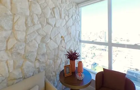 Sala de espera com parede de pedra, mesinha, poltrona e janela para a cidade